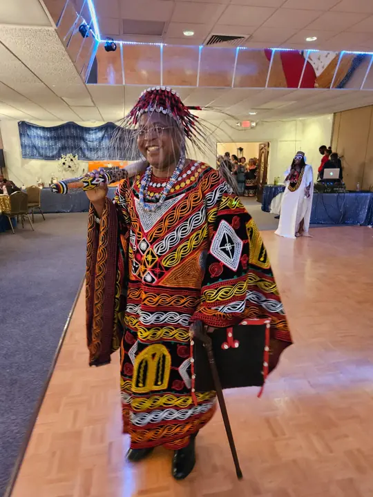 Elder in a full toghu robe and feathered headdress with a cane