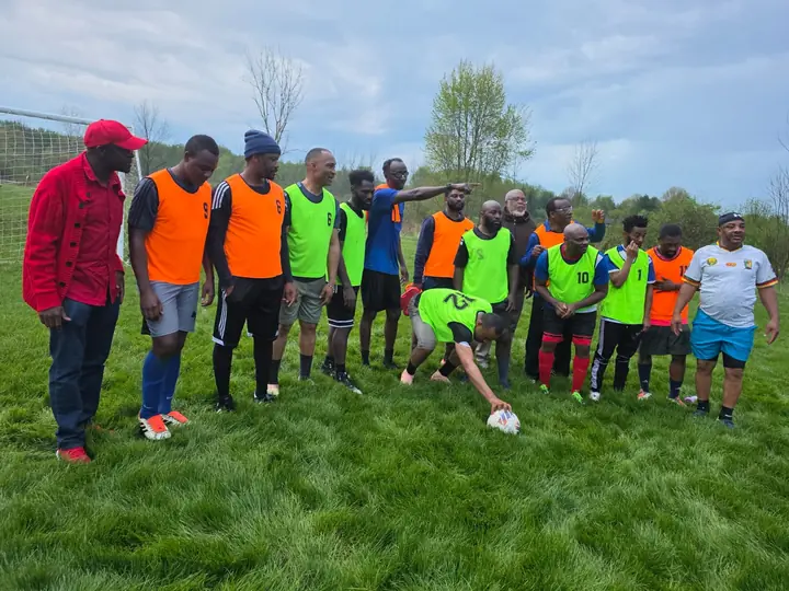 CAVFC members in training bibs gathered around the ball at an outdoor session