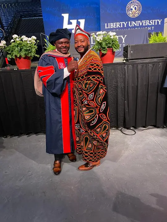 Member in graduation regalia with a member in traditional attire
